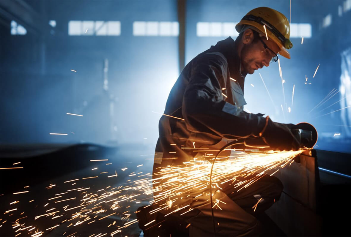 Ouvrier découpant de l'acier avec une meuleuse ou disqueuse dans un atelier industriel
